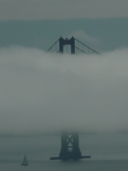 The south tower of the Golden Gate Bridge hides in a fog bank.  Note the tiny sailboat for scale.