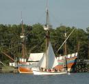 A small sailboat plies the waters in front of the Queen Elizabeth II, a reproduction of a 16th Century English sailing ship docked at Roanoke Island Festival Park.