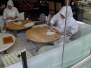 Fresh Turkish flat bread being made in this restaurant window, crowd passing on street gathered to watch, clever draw.