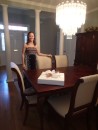 That evening, Julia proudly stands in her dining room, which has been newly cleaned and polished in honor of arriving guests. A beautifully wrapped gift symbolizes the joy and anticipation of the bride on this eve of her Wedding Day.
