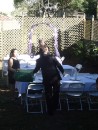 While the bride is busy standing around looking pretty for her photographs, the groom (foreground) is working hard to help set up tables and chairs for the reception dinner. (Note the purple-draped trellis in the background that served as a backdrop during the wedding.)
