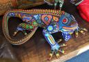 This exquisite iguana is an excellent example of the Huchol ("We-chol") native art that is very abundant around Banderas Bay. Huchol (known as the "Peyote People" because peyote is sacred to their tribe) include many animals and symbology in their designs. Brilliantly colored tiny glass beads are hand pressed one-by-one into a thin layer of bees wax covering art forms made of wood, clay, or polymer. The green "flowers" along the hind leg of this iguana and the blue one of the front shoulder symbolize peyote buttons. 