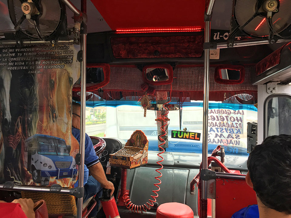 The interior of this whole bus was RED including the LED lighting that turns on when the driver presses the break-peddle. His hand-carved coin-holder is decorated with the Virgin of Guadalupe. The "TUNEL" ("toon-el") sign indicates that this is an express bus taking the highway around the back-side of PV and through the mountain tunnel to Old Town, or Zona Romantica south of downtown PV, rather than stopping at every block along the malecon (ocean-front) in town. The words written on the window (far right in photo) are the major stops it makes. We