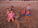 Somewhat blurry pic of some children on the beach making a sand sculpture of a mermaid.
