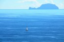 Sailboat travelling east along north shore of Hiva Oa during calm wind conditions.  The island of Fatu Huku in the background