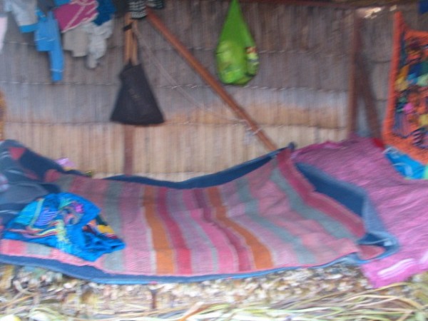 View of the inside of a house with one bed made out of reeds with a blanket on top to sleep the parents and children.  Cozy!