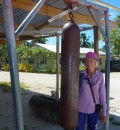 Ros itching to dong the church bell!  The traditional log drum on the ground behind her