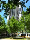 Melbourne, characterized by a city bus passing a tall building among green trees. 