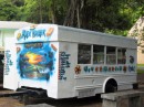 Alex Trailer, a hippie-style fast food bus, sits in the shade of a large tree near the Executive Office building.
