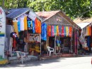 A row of tropical shops displaying colorful wares lines the hill leading down to the beach. (Sosua, Dominican Republic)